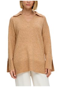 Maglione oversized beige con scollo a V e colletto, caratterizzato da polsini e orli a coste. La texure appare morbida e calda.