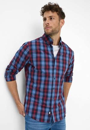 Geruite blouse met rode, blauwe en witte patronen, met een knoopsluiting bij de kraag, lange mouwen opgerold, gemaakt van een lichte stof.
