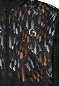 Gevoerde jas van gestructureerde zwarte stof met een diagonaal oranje en witte geometrische patroon, voorzien van een voorrits en logo-detail.