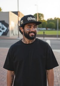 Musta t-paita lyhyillä hihoilla, jonka päällä on henkilö. Mustassa lippiksessä on kohotettu teksti "69ers" hopeisena. Huomattavat kasvojen tatuoinnit ja parta.