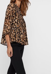 Blouse en imprimé floral abstrait noir et marron avec des manches trois-quarts et un col froncé, associée à un pantalon noir ajusté.