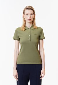 Olivgrön polotröja med krage, korta ärmar, knapplist och en broderad logotyp på vänster bröst.