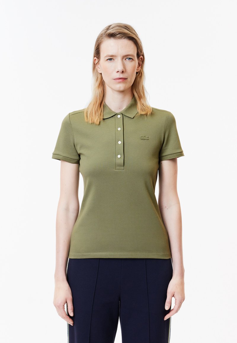 Olivgrön polotröja med krage, korta ärmar, knapplist och en broderad logotyp på vänster bröst.