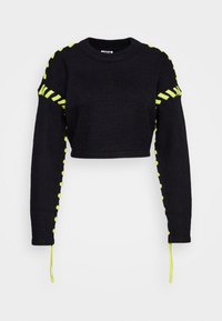 Svart kort tröja med långa ärmar, prydd med neongul snörning längs ärmarna och axelsömmarna. Stickad textur, rund halsringning.