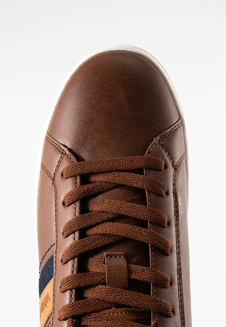 Zapatilla de cuero marrón con un acabado texturizado, presenta cordones marrones y una suela de goma blanca. Incluye un acento de tela azul y un detalle de logo.