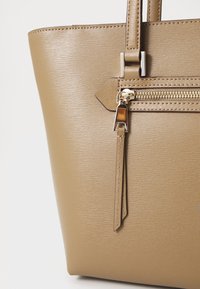 Tan synthetic tote bag with textured finish, featuring elongated handles, a zippered pocket with gold hardware, and a rectangular shape.