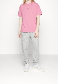 Ljusrosa crewneck t-shirt med liten logotyp, tillsammans med grå sweatpants med en diagonalt placerad logotypdesign, och vita sneakers.