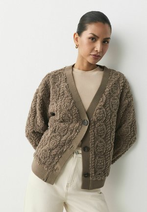 Cardigan bej cu textură căruntă, cu o suprafață pufoasă, mâneci și tiv cu nervuri, și nasturi închisi la culoare. Purtați peste un top bej, asortat cu pantaloni deschiși.
