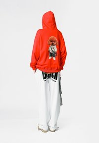 Sudadera roja con capucha que presenta un gráfico de un perro de dibujos animados en la parte posterior. Combinada con pantalones de chándal blancos de corte holgado que exhiben letras negras.