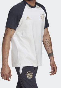 Pánský dres s krátkým rukávem v bílé barvě s námořnickými rukávy, s zlatým logem Adidas a vyšitým logem FC Bayern München na hrudi.