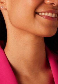 Close-up van een gladde, warmgetinte nek met een opvallende sleutelbeen, die een kleine zilveren stud oorring draagt, tegen een felroze kledingstuk.