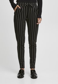Svarta randiga byxor med tunna, beige vertikala linjer. Tillverkade av mjukt tyg, med dragsko i midjan och sidofickor.