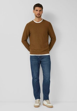 Brown long-sleeve sweater with white collar, blue jeans, and cream sneakers. Features textured fabric and fitted silhouette.
