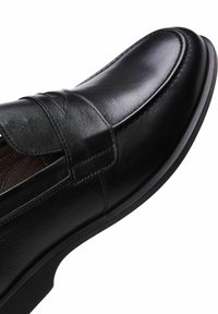 Zwarte leren schoen met een gladde afwerking, een ronde neus en een decoratieve band over de bovenkant met subtiele stikdetails.