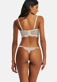 Ensemble de lingerie en dentelle beige comprenant un bralette avec un motif floral et des bretelles réglables, associé à un string assorti.