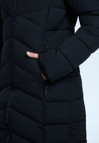 Černá péřová bunda s prošívaným designem a diagonálním švem, se zipem vpředu a bočními kapsami. Látka vypadá hladce a jemně.