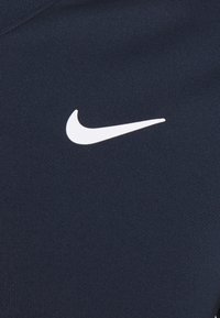 Tela azul marino con una textura suave que presenta el logotipo de la marca Nike en color blanco. El diseño es minimalista, centrándose en el logotipo como un detalle clave.