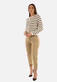 Giacca a righe corta in crema e blu navy, abbinata a pantaloni cargo beige con tasche e dettagli con cerniera agli orli; tacchi neri.