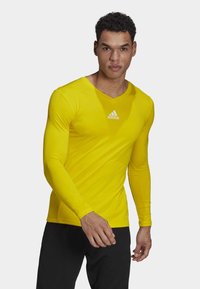 Langarmige gele shirt gemaakt van een gladde, rekbare stof. Heeft een V-halsontwerp en een klein wit Adidas-logo op de borst.