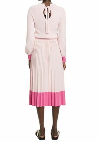 Robe en tricot côtelé rose clair avec des manches longues, jupe plissée et ourlet rose. Présente une ouverture en forme de clé au dos avec un lien.