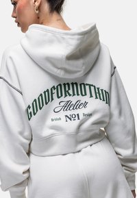 Witte hoodie met een grote groene afbeelding met de tekst "GOODFORNOTHING" en "Atelier No1 British Design" op de achterkant. Voorzien van een te strikken capuchon.