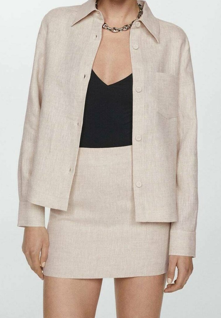 Camicia button-up in lino beige con colletto, abbinata a una gonna fitted coordinata. Top nero sotto, con un dettaglio tasca discreto sulla camicia.