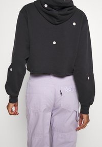 Schwarzer, kurzer Hoodie mit bestickten Gänseblümchen-Akzenten; kombiniert mit hellvioletten Cargohosen mit aufgesetzten Taschen und Markenlogo.