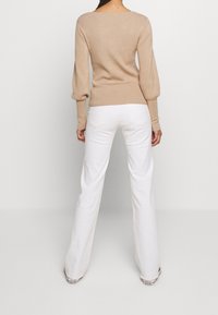 Suéter beige acanalado con mangas abullonadas, combinado con vaqueros blancos acampanados. El suéter cuenta con un escote amplio y un diseño ajustado.