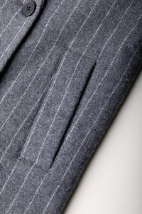 Blazer gri din lână cu un model fin în dungi, închidere cu un singur nasture și un buzunar cu flaps. Materialul are o textură fină.