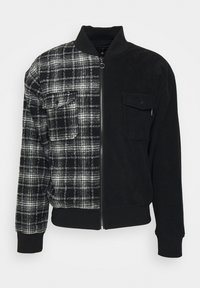 Veste à carreaux noirs et gris avec fermeture éclair intégrale, col et poignets côtelés, et poches poitrine à l'avant de chaque côté.