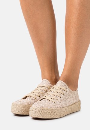 Baskets en dentelle beige avec une semelle en jute tissée, présentant un motif floral et des lacets neutres. Texture lisse dans l'ensemble, design discret.