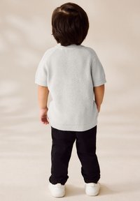 Grauer gestrickter Pullover mit kurzen Ärmeln und geripptem Kragen, kombiniert mit schwarzen Hosen und weißen Turnschuhen. Das Kind zeigt dem Betrachter den Rücken.