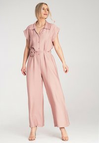 Różowy kombinezon z szerokimi nogawkami, wykonany z lekkiego materiału, z kołnierzykiem, krótkimi rękawami, guzikami z przodu oraz dekoracyjnym kwiatowym akcentem w talii.