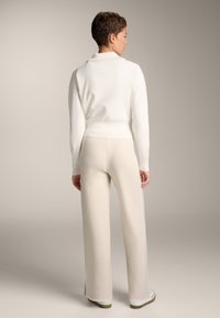 Weißer gestrickter Pullover mit umgeschlagenem Kragen, kombiniert mit cremefarbenen, weiten Hosen mit seitlichen Schlitzen, was eine sanfte, schlanke Silhouette erzeugt.