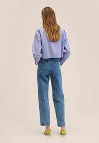 Camisa a rayas azul y blanca, con mangas holgadas, combinada con unos vaqueros de cintura alta de color azul claro. Sandalias de tacón amarillas completan el look.