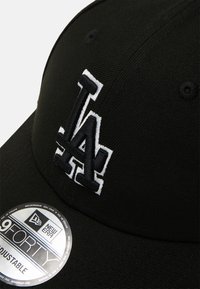 Căciulă de baseball neagră, confecționată dintr-un material structurat, având un logo alb brodat "LA". Include un autocolant circular New Era pe bordură.