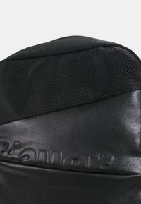 Zaino nero con un materiale superiore testurizzato e una sezione inferiore liscia. Presenta un logo in rilievo e una chiusura a zip anteriore.