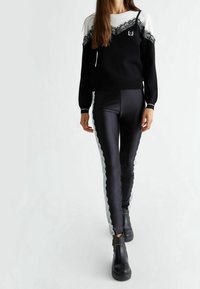 Pull noir et blanc avec détails en dentelle et logo, associé à un pantalon noir en satin avec accents en dentelle sur les côtés. Bottines noires.