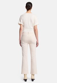 Jean évasé couleur crème à taille haute, avec un design à cinq poches et une texture douce. Le modèle porte un haut crème à manches courtes.