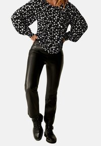 Czarna bluzka z długim rękawem w biały wzór gwiazdek, zestawiona z dopasowanymi czarnymi skórzanymi spodniami i czarnymi botkami na sznurowadła. Gładka faktura i dopasowany krój.