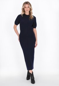 Rochie tricotată neagră cu dungi, cu un corset ajustat și fustă lungă, având un decolteu rotund și mâneci scurte, asortată cu botine negre.