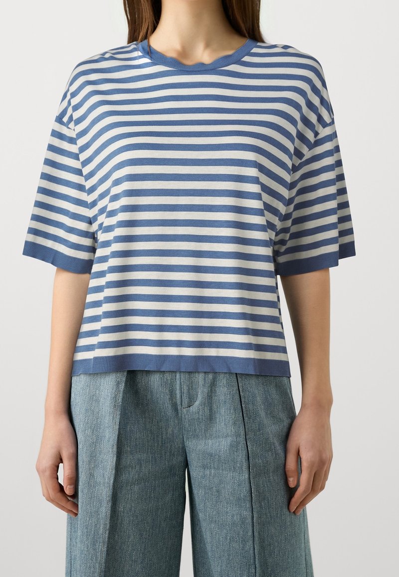 Pasiasta niebiesko-kremowa, oversize'owa koszulka z krótkim rękawem, żebrowanym dekoltem i skróconym fasonem, w komplecie z jasnoniebieskimi, teksturowanymi spodniami.