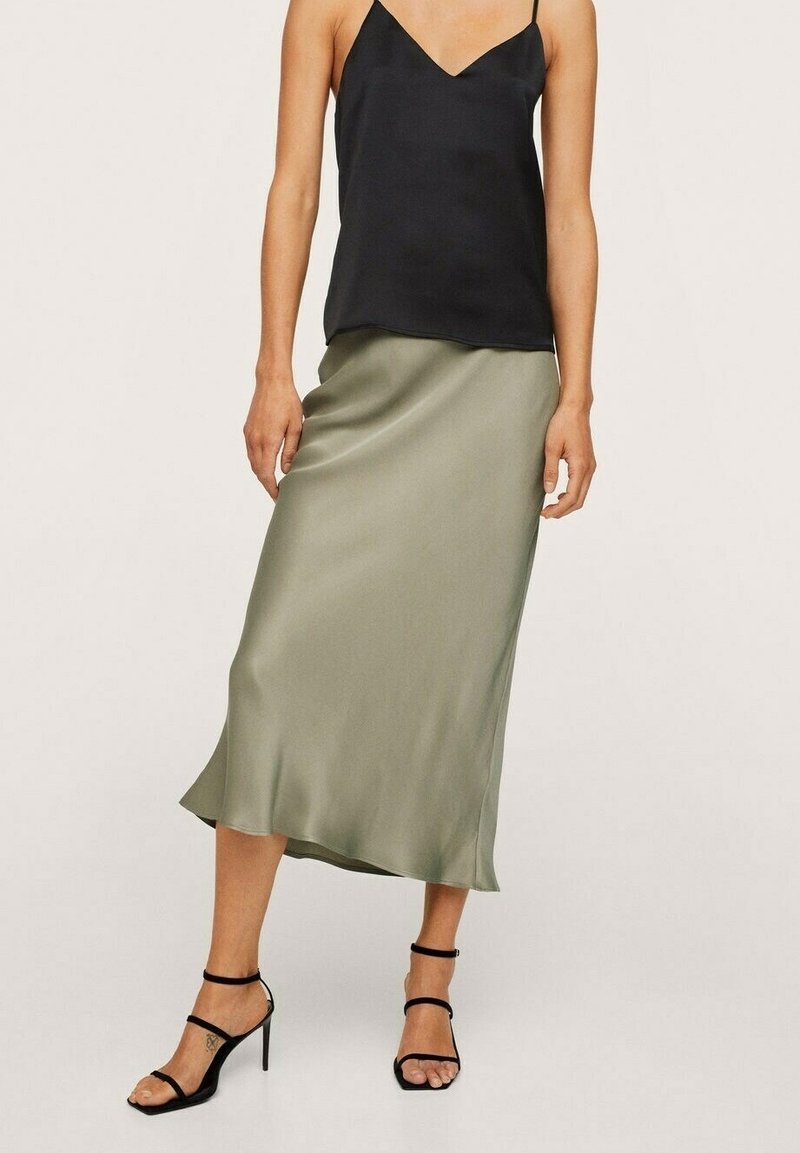 Femme portant un haut noir sans manches assorti à une jupe midi taille haute en satin vert olive et des sandales noires à talons hauts et lanières.