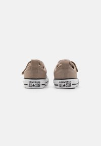 Smeđe platnene tenisice niskog profila s bijelim gumenim potplatima, s crnim prugama i oznakom "CONVERSE ALL STAR" na peti. Klasični sustav vezanja.
