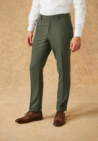 Pantalons habillés texturés verts avec une coupe slim, dotés d'une taille avec passants de ceinture, associés à des chaussures habillées marron.