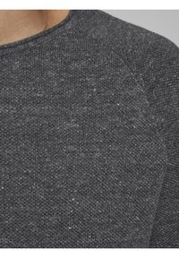 Tessuto lavorato a maglia grigio scuro con una superficie strutturata. Presenta un collo rotondo e maniche raglan, incorporando sfumature più chiare nel materiale.