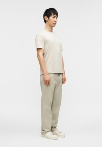 Ανοιχτό μπεζ κοντομάνικο πουκάμισο με διακριτικό σχέδιο, σε συνδυασμό με φωτεινό γκρι παντελόνι και κρεμ αθλητικά παπούτσια. Μινιμαλιστικός σχεδιασμός, άνετη εφαρμογή.