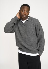 Grå ribbet sweater med krave, lange ærmer og en afslappet pasform, lagd over en hvid t-shirt. Ingen bemærkelsesværdige mønstre eller accenter.