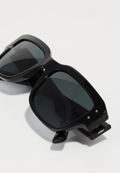 Black square sunglasses with dark lenses. Glossy plastic frame featuring metallic accents and a distinct hinge design.