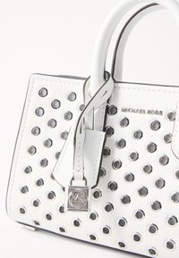 Borsa a mano bianca in pelle con dettagli in occhietti argentati, dotata di manici doppi e di una targhetta pendente con il logo MK. Texture liscia.